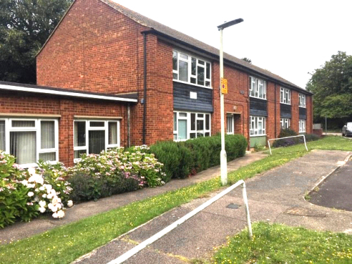 Two storey and single storey red brick accommodation with grass and path outside.