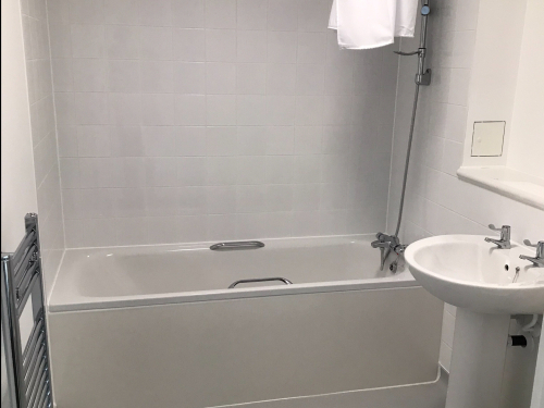 White modern bathroom including bath with overhead shower, sink and toilet.