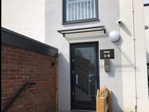 Photograph of steps up to glass door in modern white building with window above.