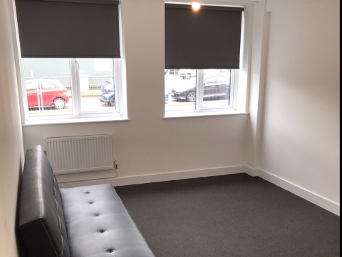 Small modern room with two windows, white walls and small leather sofa.