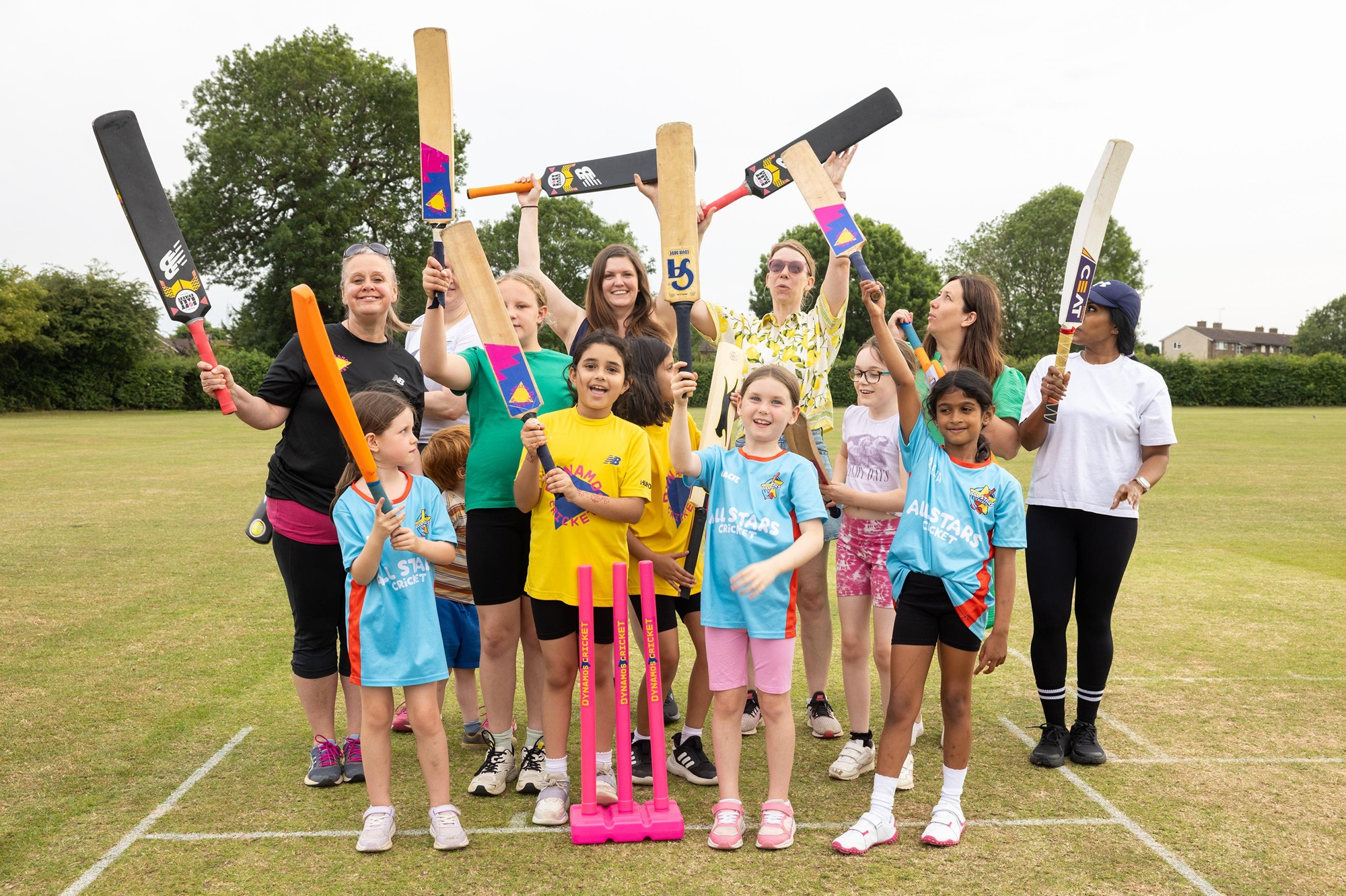 Group of girls standing on playing field waving cricket bats